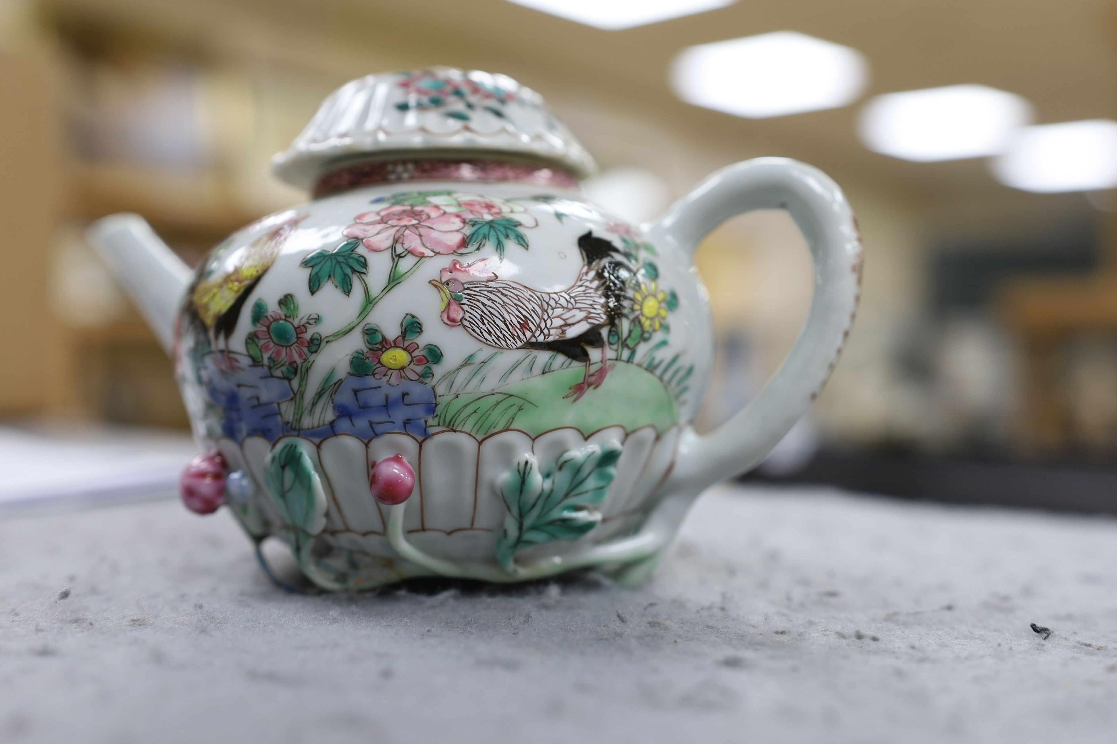 A Chinese famille rose chrysanthemum moulded teapot, early Qianlong period, painted with a cockerel amongst flowers, on a cage work base, 10 cms high